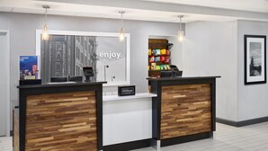 A hotel reception desk with a modern design, featuring a wood panel accent, a framed cityscape, and a vending machine stocked with snacks. - Hampton Inn & Suites Parsippany/North (Parsippany)
