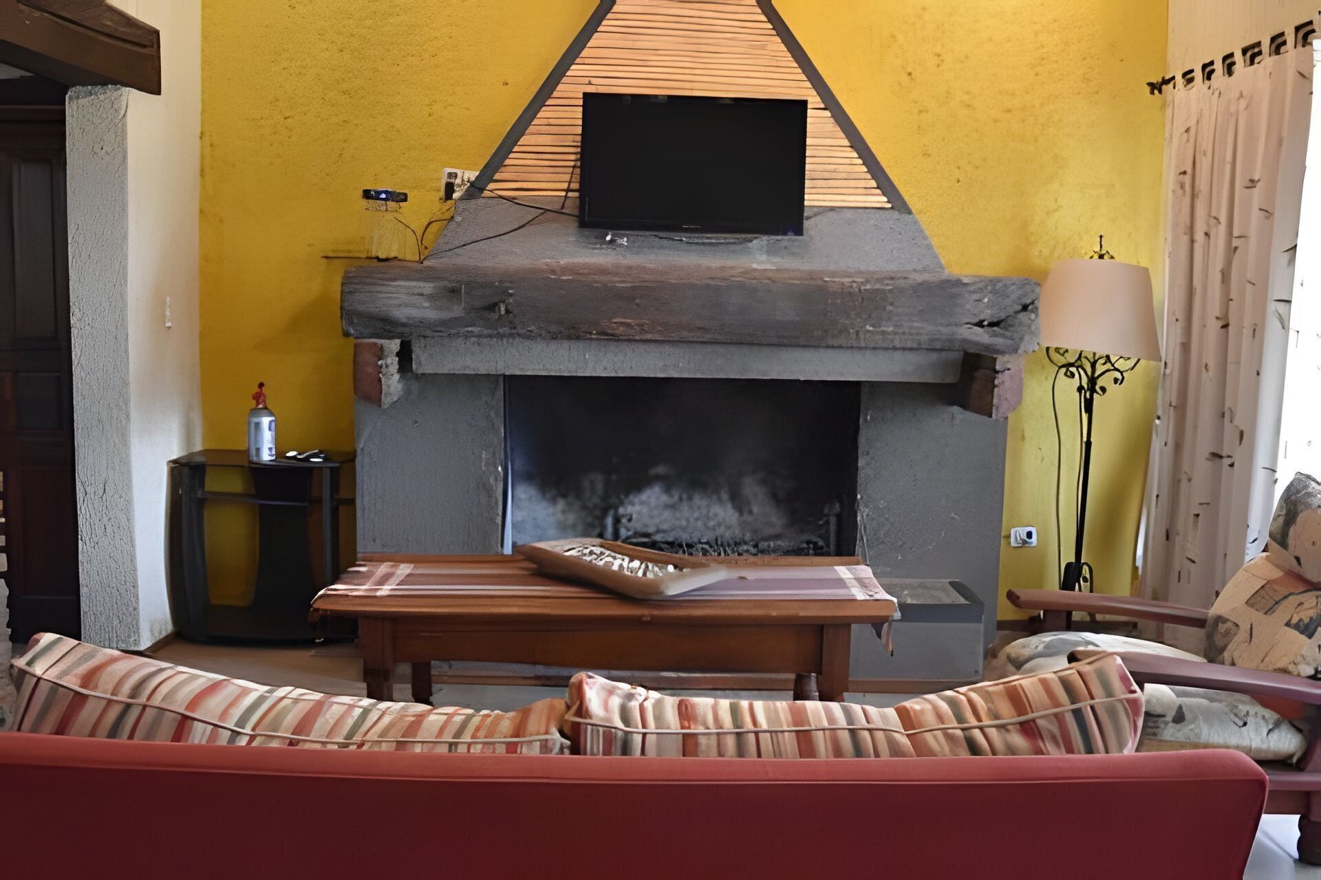 Una sala de estar con chimenea, un sofá y un televisor colocado encima de la chimenea.