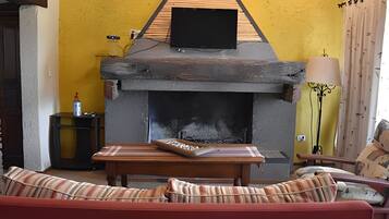 Una sala de estar con chimenea, un sofá y un televisor colocado encima de la chimenea.