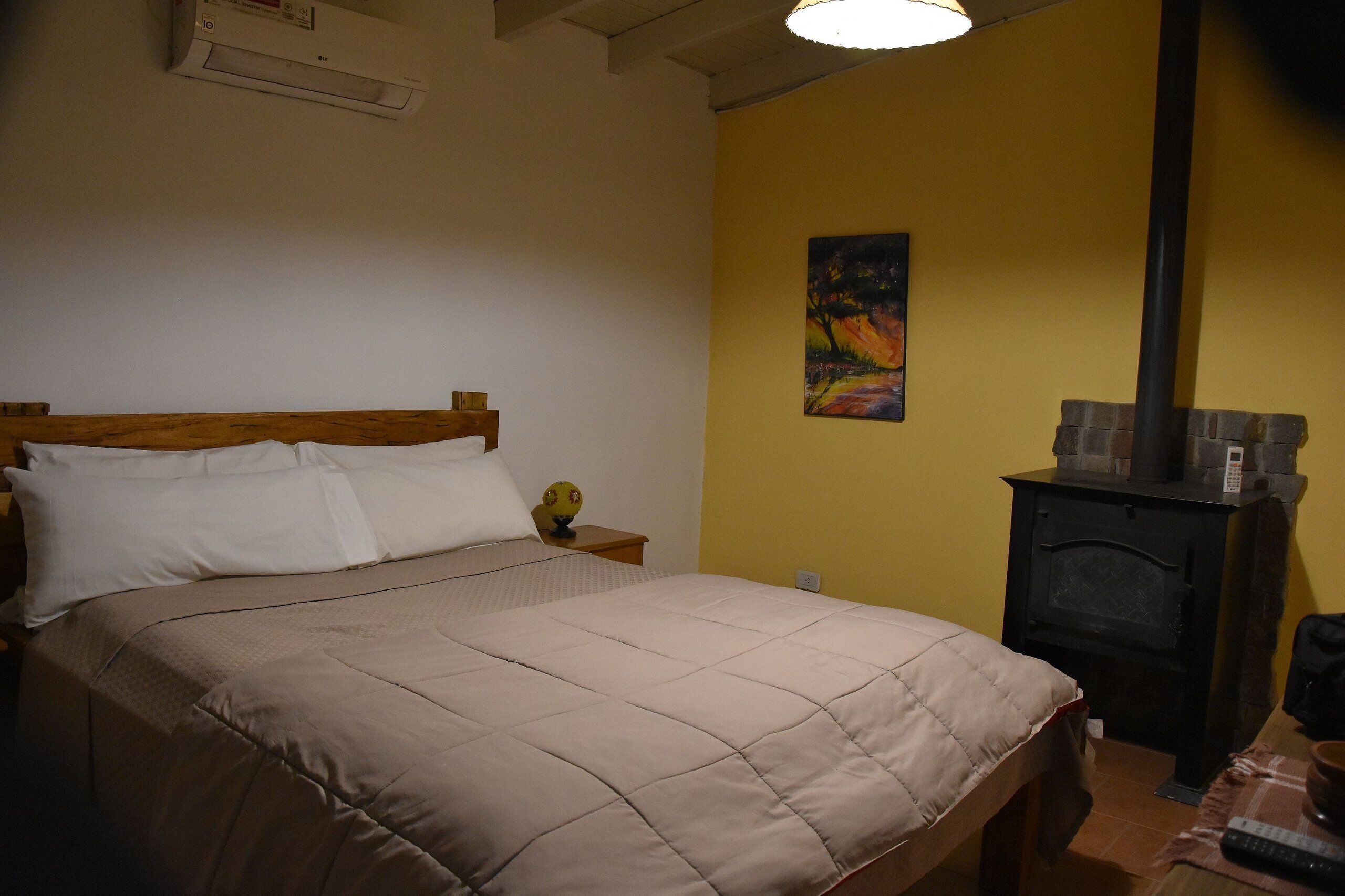 A bedroom with a bed, a nightstand, a painting, a fireplace, and a remote control.