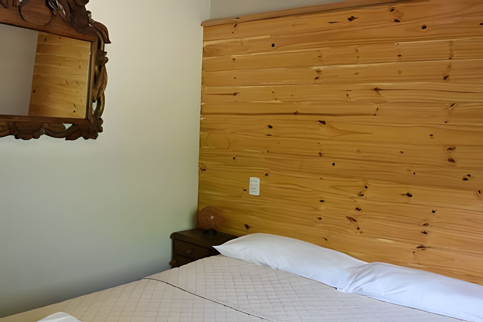 Een kamer met een houten hoofdbord, een nachtkastje en een spiegel.