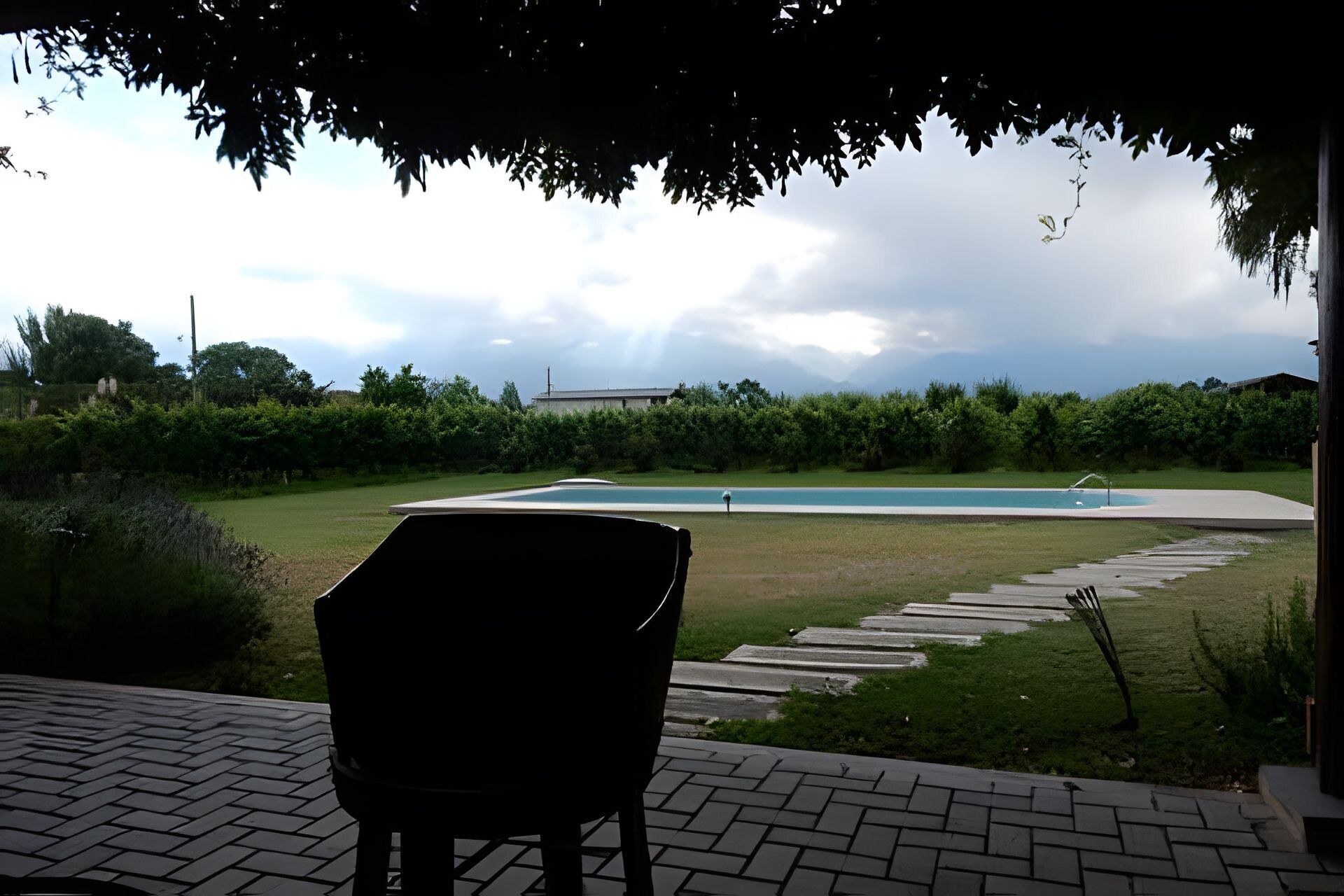 Un patio con vistas a una piscina, rodeado de vegetación y un camino de ladrillo.