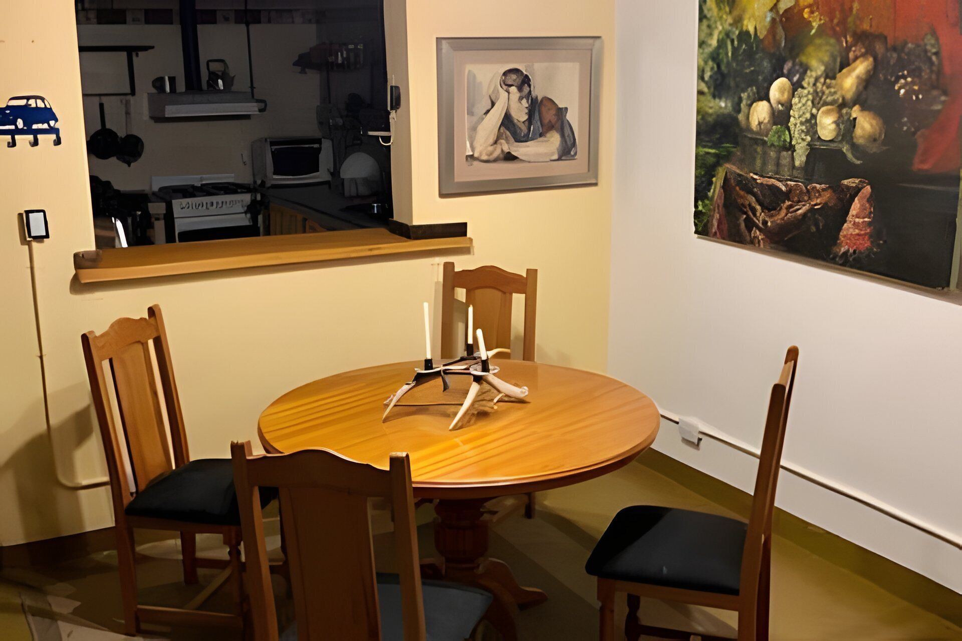 Un comedor con una mesa redonda de madera, cuatro sillas de madera con asientos acolchados, un cuadro enmarcado en la pared y un espejo que refleja la habitación.