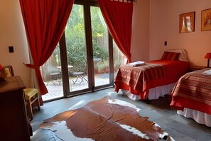 A bedroom with a large glass door leading to an outdoor area, a bed with red bedding, and a cowhide rug on the floor. - Finca Ogawa (Tunuyan)