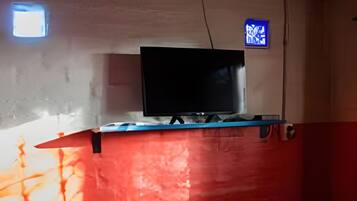 Habitación con televisión montada en una pared roja, una mesita con un jarrón y una ventana con luz azul.