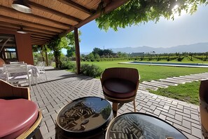 An outdoor seating area with chairs and tables, a wooden pergola, and a view of a landscaped garden and mountains in the distance. - Finca Ogawa (Tunuyan)
