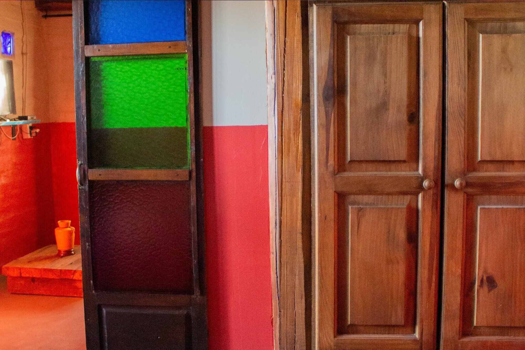 Una puerta de madera con diseño de panel, una pared roja y blanca, y un panel verde y negro.