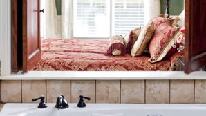 Una camera da letto con un'ampia finestra, un letto con biancheria rossa, una lampada e una vasca da bagno.