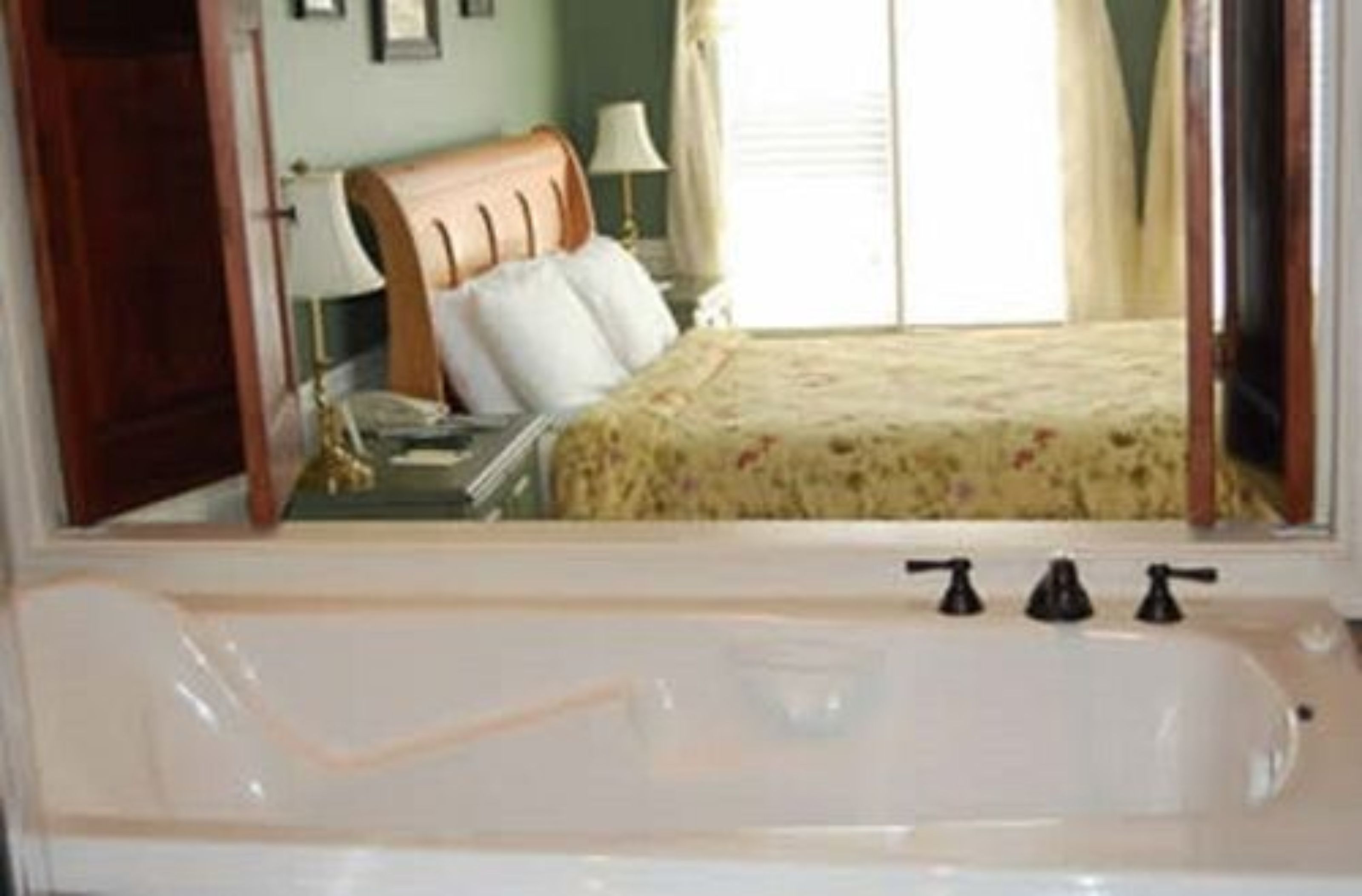 Una camera d'albergo con una vasca da bagno ampia, una testiera in legno e un letto con copriletto floreale.