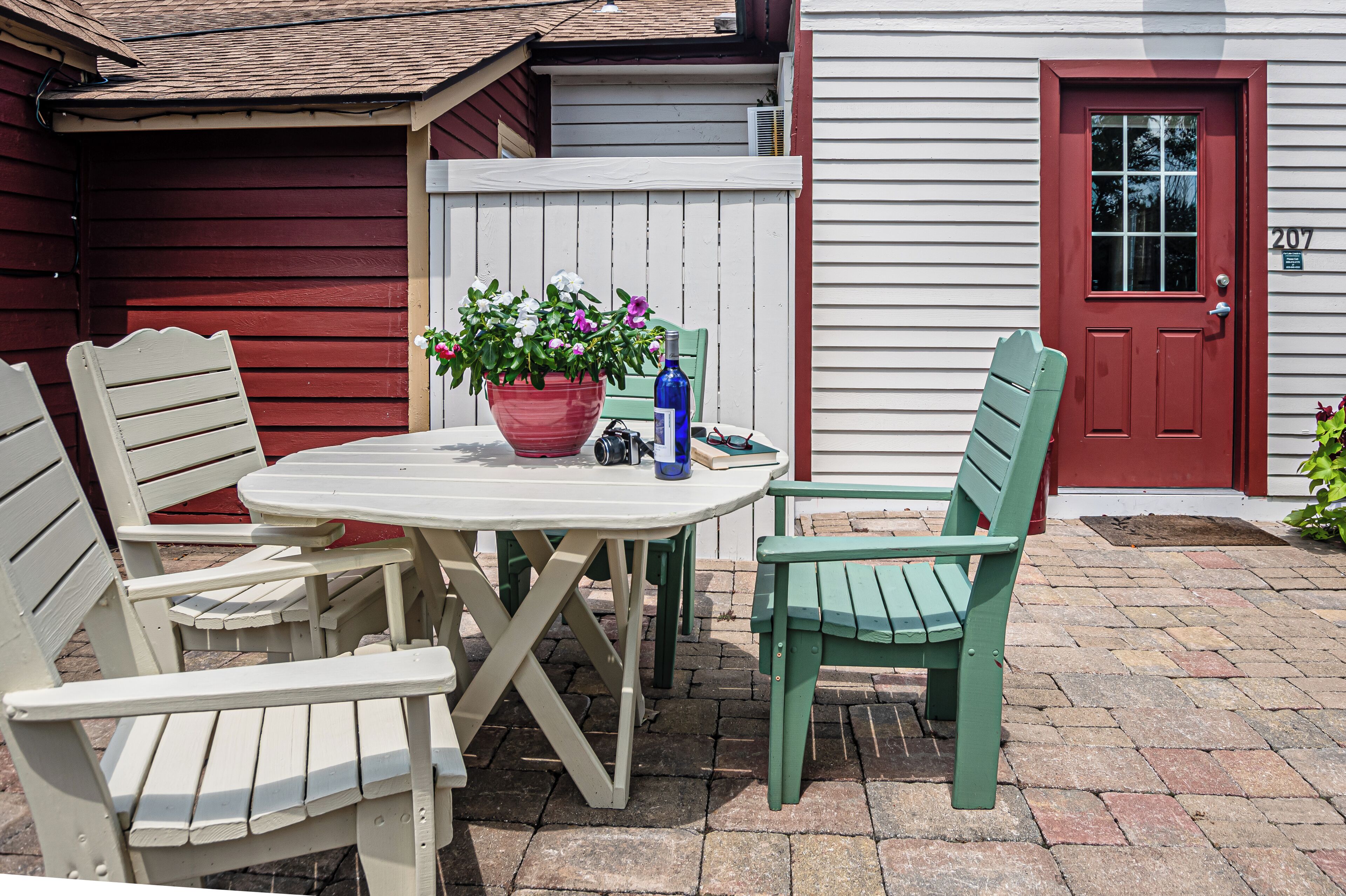 A patio with a white table and two chairs, a potted plant, and a bottle.