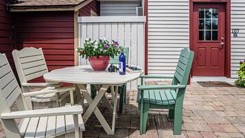 A patio with a white table and two chairs, a potted plant, and a bottle.