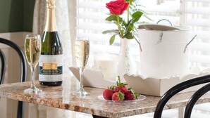 Un tavolo con una bottiglia di champagne, due bicchieri, un vaso con una rosa rossa e una ciotola di fragole.