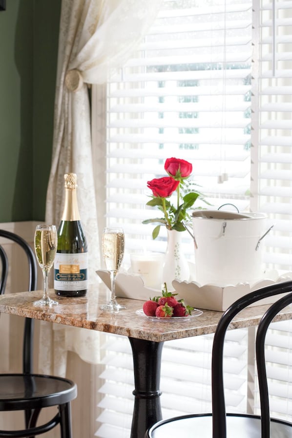 A table with a bottle of champagne, two glasses, a vase with a red rose, and a bowl of strawberries.