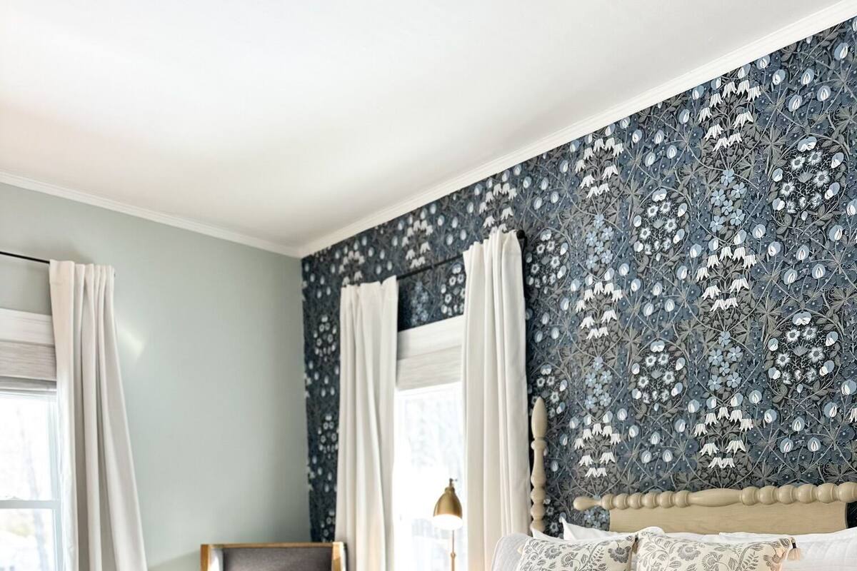 A bedroom with a large bed, a headboard, a nightstand, and a window with curtains.