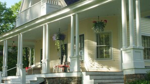 A two-story house with a porch, stone foundation, and a hanging flower basket. - Noble House Inn (Bridgton)