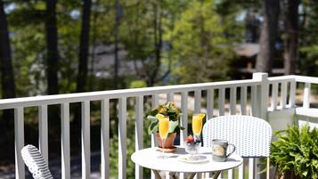 A small round table with a white tablecloth, two glasses of orange juice, a bowl of fruit, and a mug on a balcony with white railings.