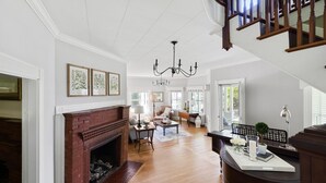 A spacious living room with a fireplace, a chandelier, and a staircase. - Noble House Inn (Bridgton)