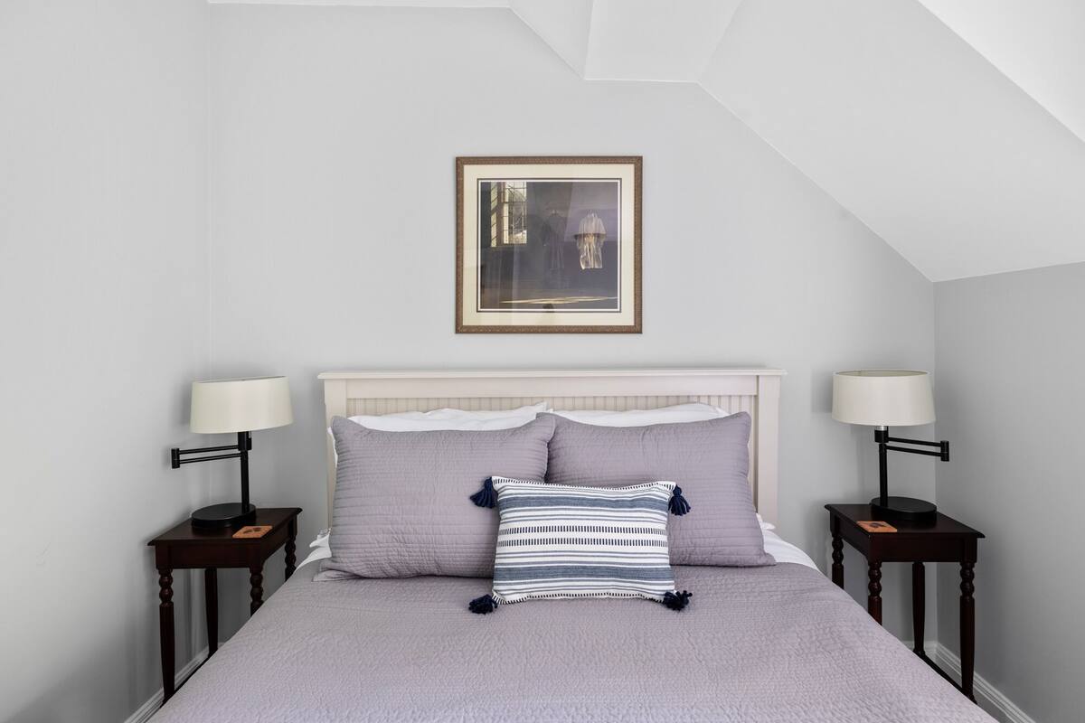 A bedroom with a bed, two nightstands, a framed picture, and a ceiling with a skylight.