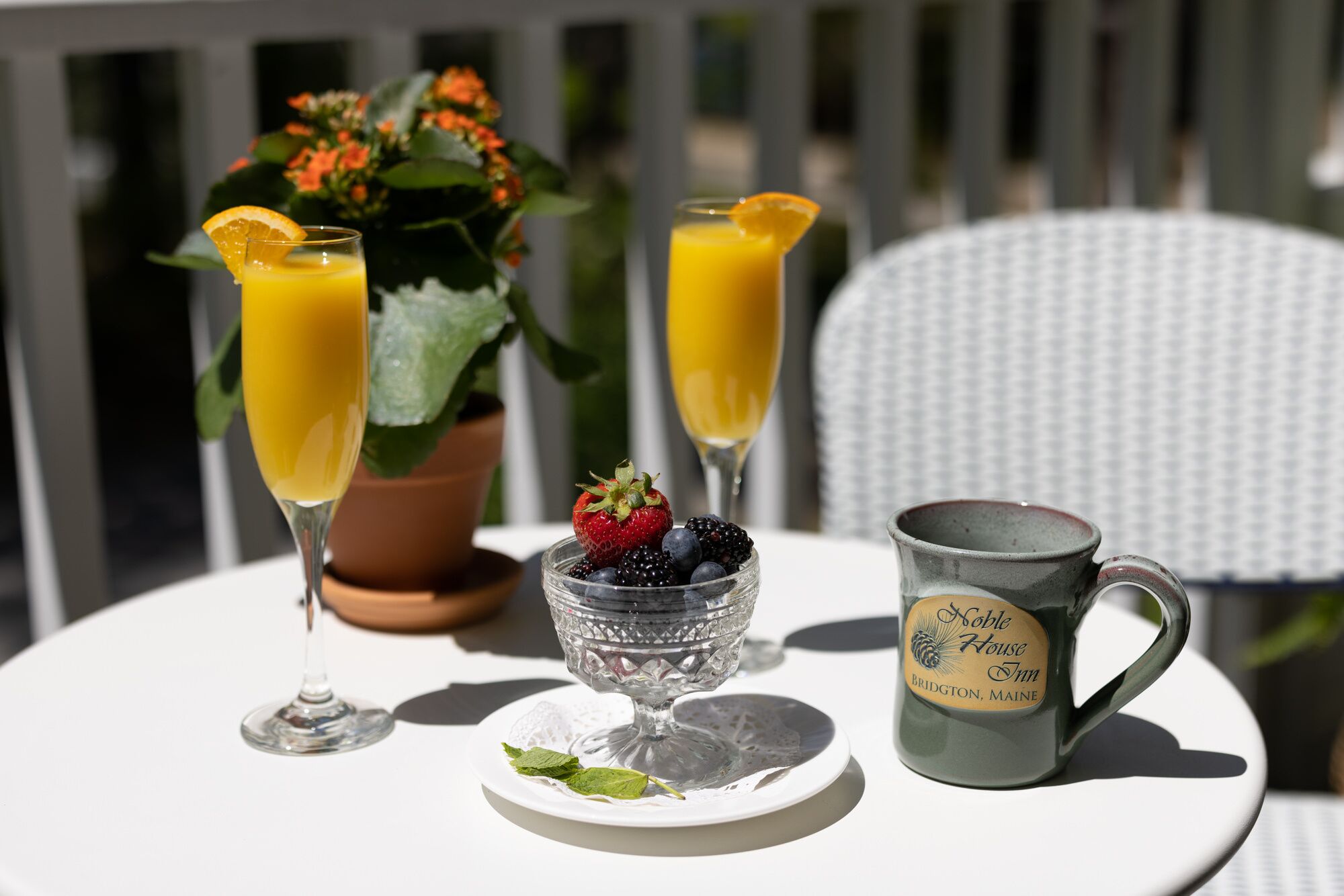 Uma mesa com dois copos de suco de laranja, uma tigela de frutas vermelhas e uma caneca com etiqueta.