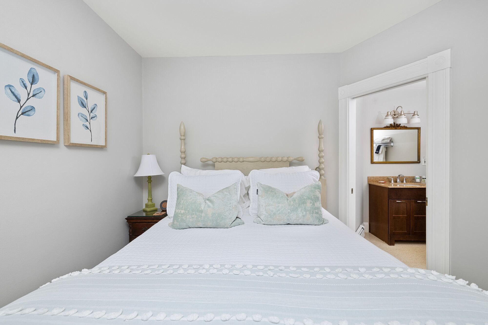 A bedroom with a bed, two pillows, a nightstand with a lamp, and a framed picture on the wall.