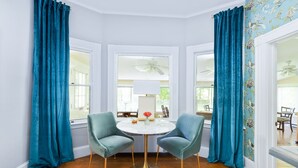 A dining room with a round table, two chairs, and teal curtains. - Noble House Inn (Bridgton)