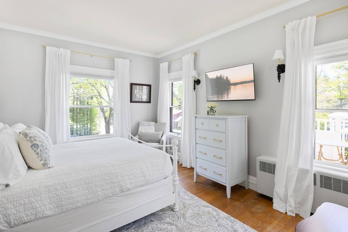 A bedroom with a bed, a dresser, a chair, a TV, and a window with curtains.
