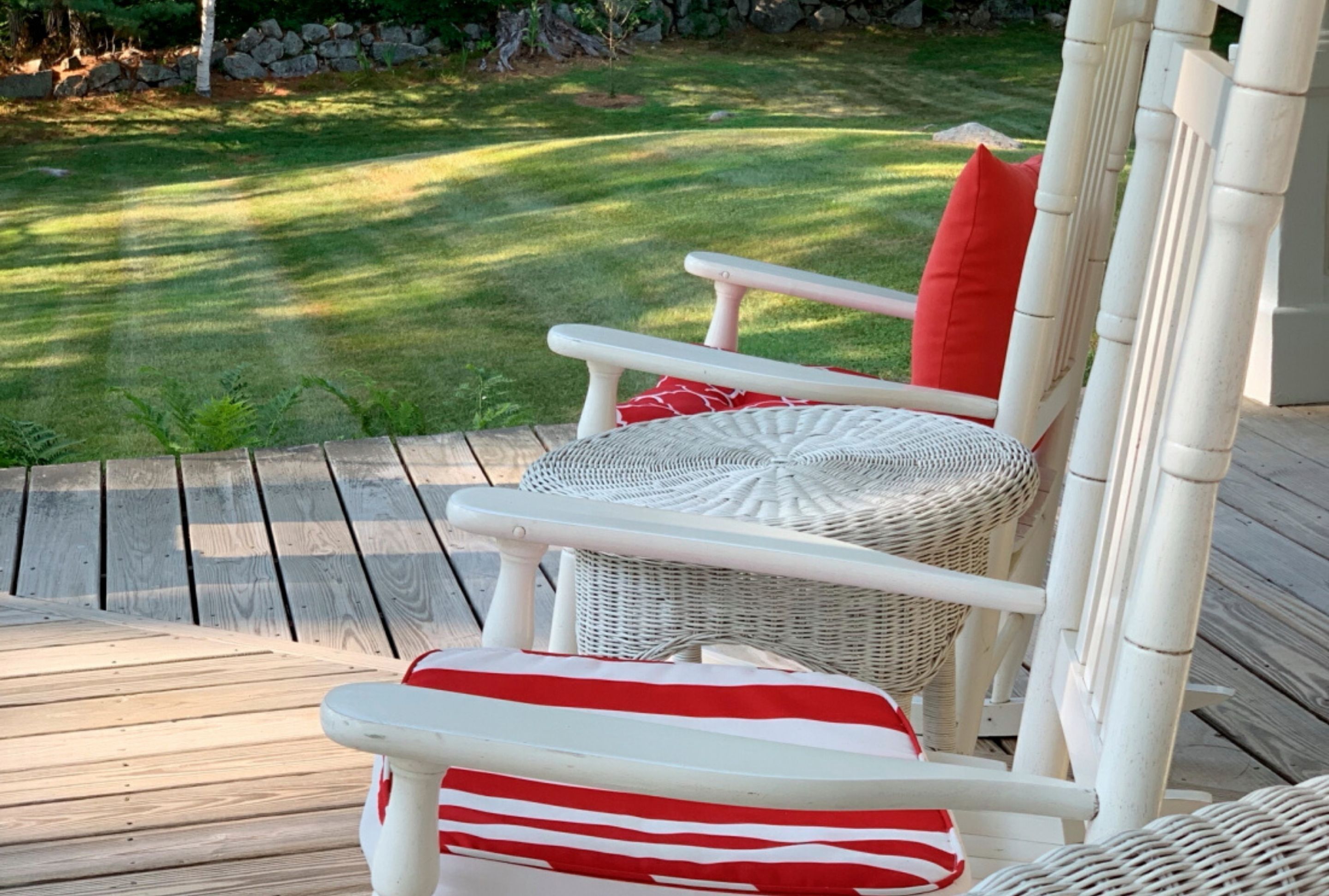 Una silla de mimbre blanca con un cojín rojo sobre una terraza de madera.