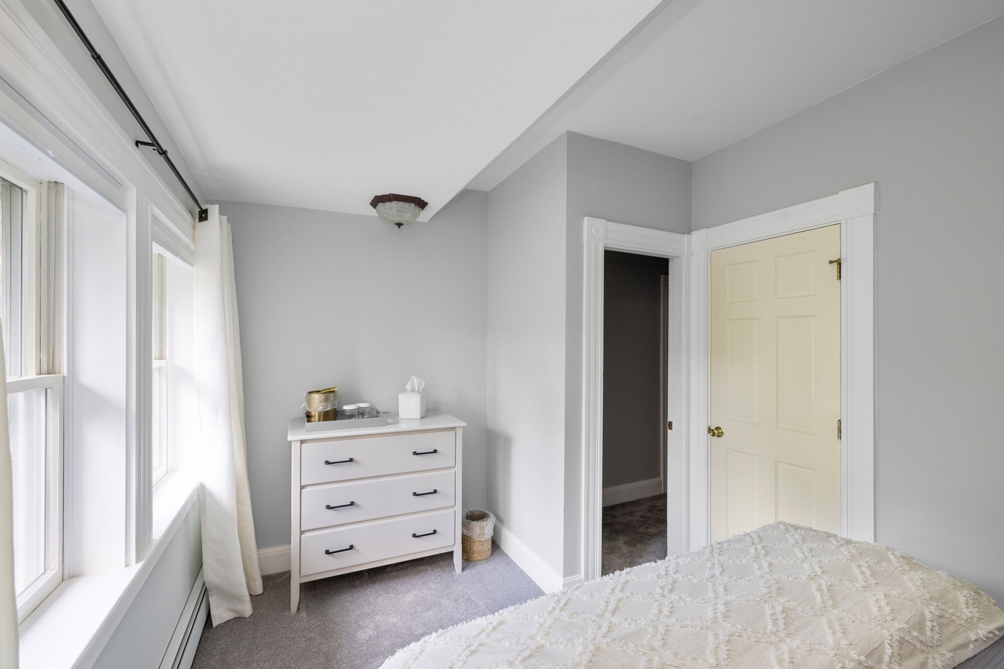 A bedroom with a white dresser, a bed, and a door leading to another room.