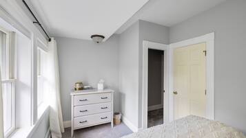 Une chambre avec une commode blanche, un lit et une porte donnant sur une autre pièce.
