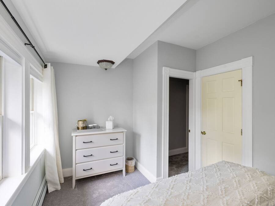 A bedroom with a white dresser, a bed, and a door leading to another room.