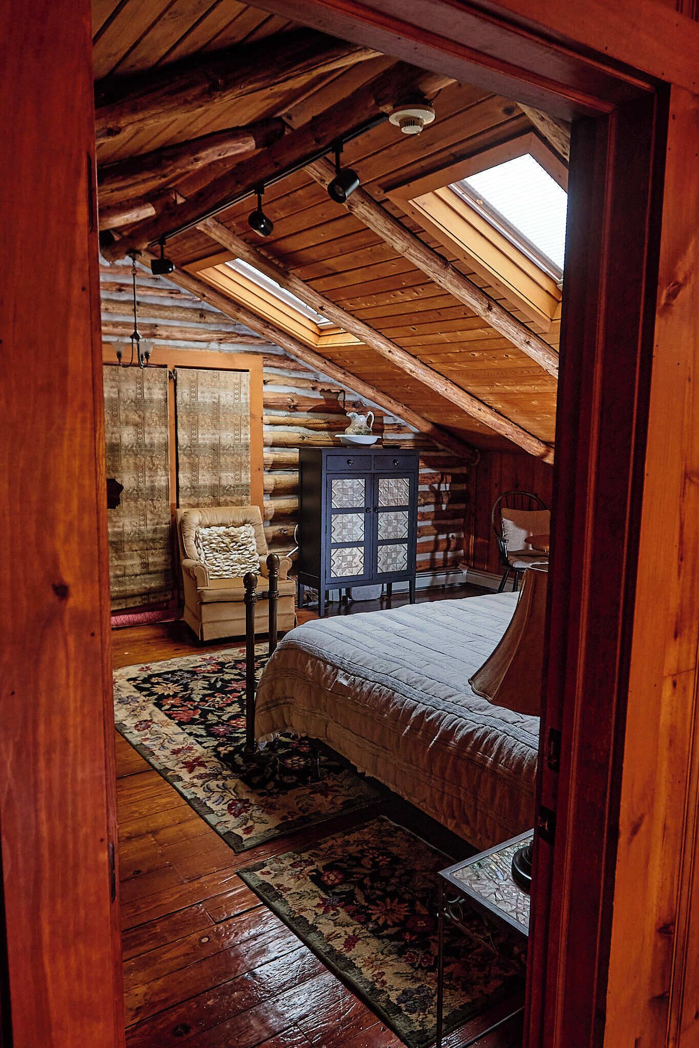 Une chambre dans une cabane en rondins, avec un lit en mezzanine, un plafond en bois et un puits de lumière.
