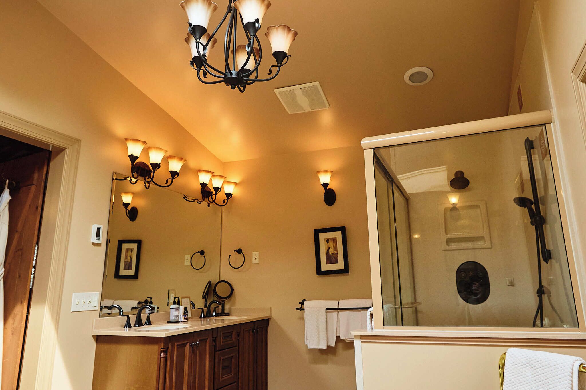 Une salle de bain dotée d’un grand miroir, de plusieurs appliques murales, d’un espace douche et de meubles en bois.