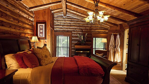 A log cabin bedroom with a large bed, wooden walls, a chandelier, and a fireplace. - Chalet of Canandaigua (Canandaigua)