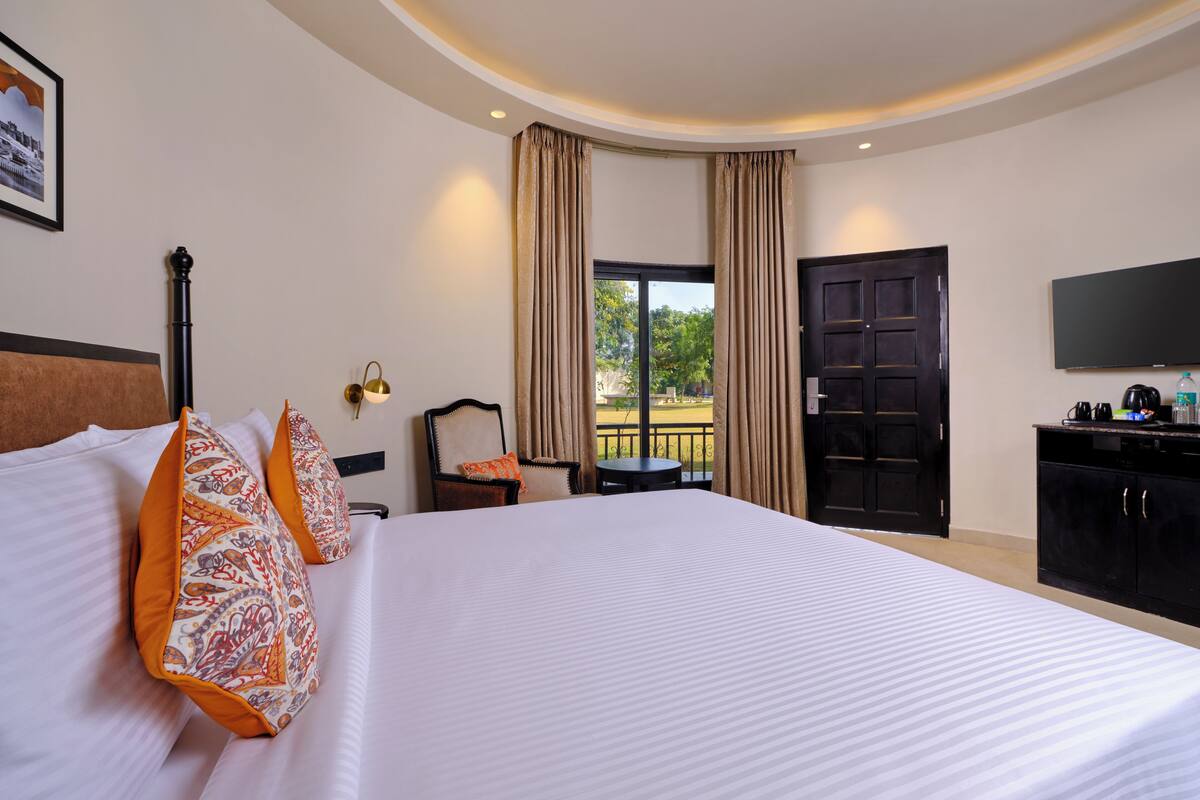 Quarto de hotel com uma cama grande, uma escrivaninha, uma cadeira, uma televisão e vista para o exterior.