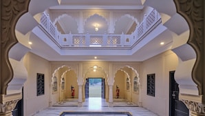 Un'imponente sala con pavimento in marmo, archi bianchi decorati e un balcone centrale con ringhiere elaborate.