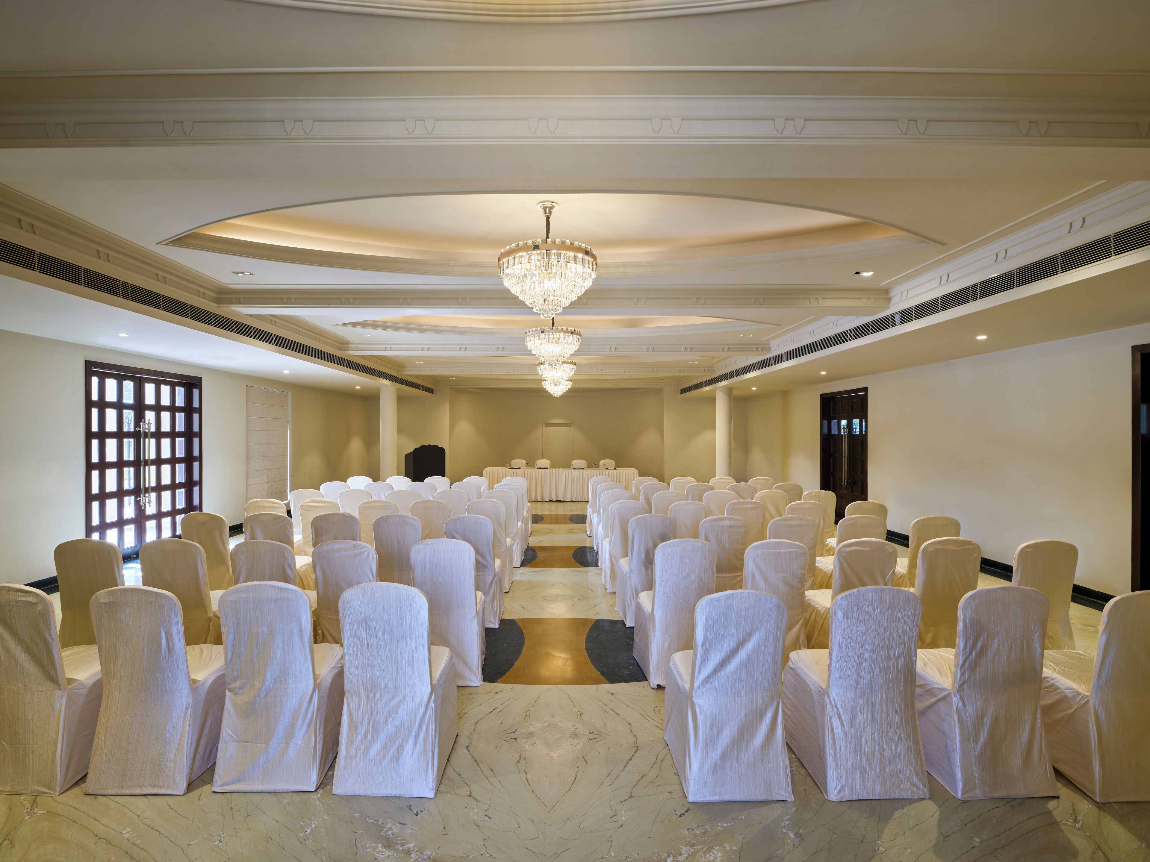 A conference room with rows of chairs covered in white fabric, a large chandelier, and a marble floor.