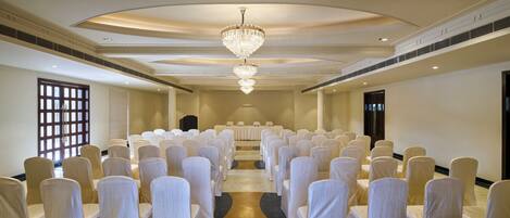 A conference room with rows of chairs covered in white fabric, a large chandelier, and a marble floor.