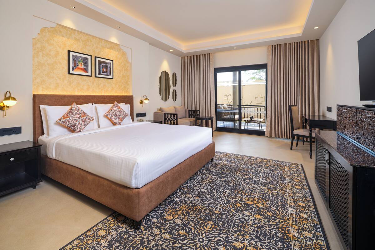 Quarto de hotel moderno com uma cama grande, uma escrivaninha, uma televisão e uma varanda com cortinas.