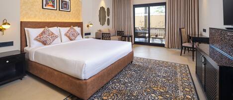 A modern hotel room with a large bed, a desk, a TV, and a balcony with curtains.