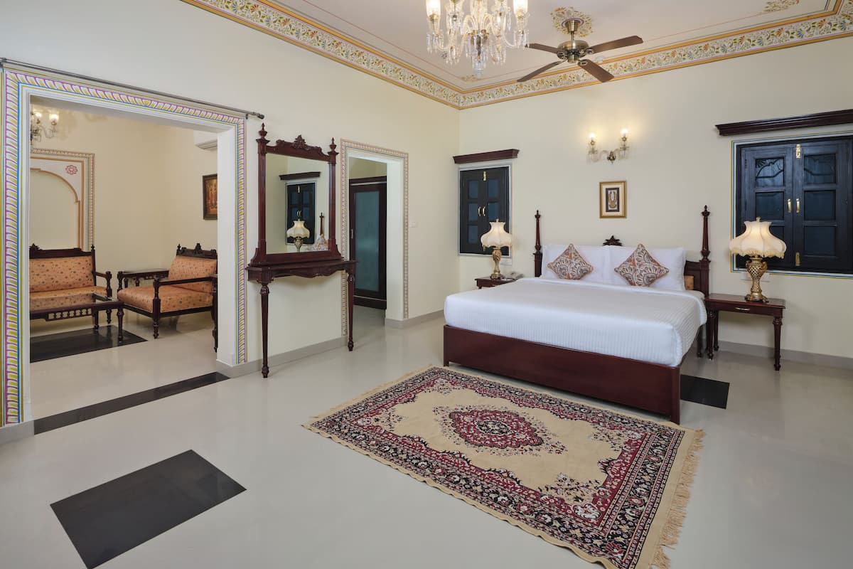 Um quarto espaçoso com uma cama grande, um espaço de estar com cadeiras, um lustre e um ventilador de teto.