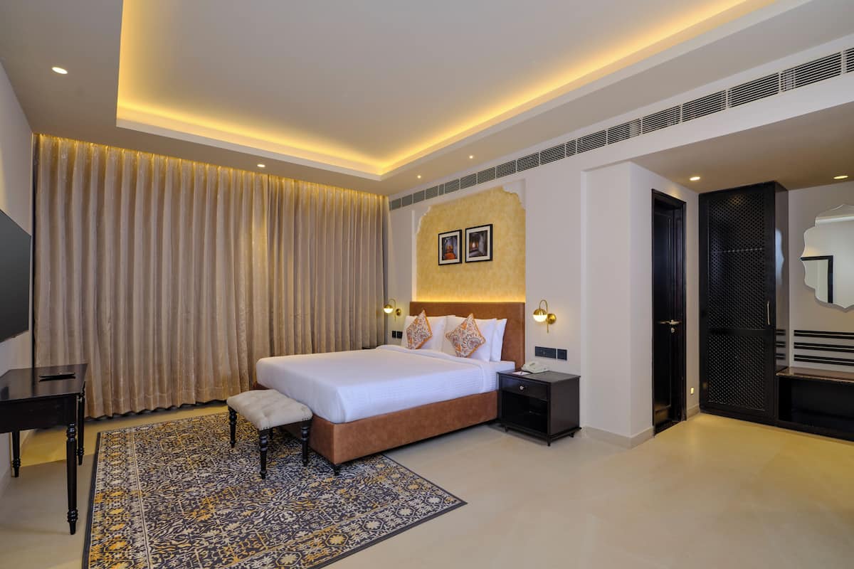 Quarto de hotel moderno com uma cama grande, uma mesinha de cabeceira, uma televisão e um tapete estampado.