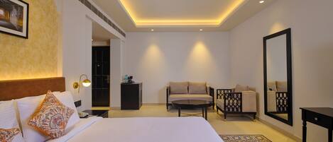A modern hotel room with a large bed, a sofa, a small table, a mirror, and a patterned rug.