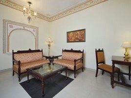 Quarto com dois sofás, uma mesa de centro de vidro, uma mesinha de apoio, um abajur, um quadro e decoração no teto.