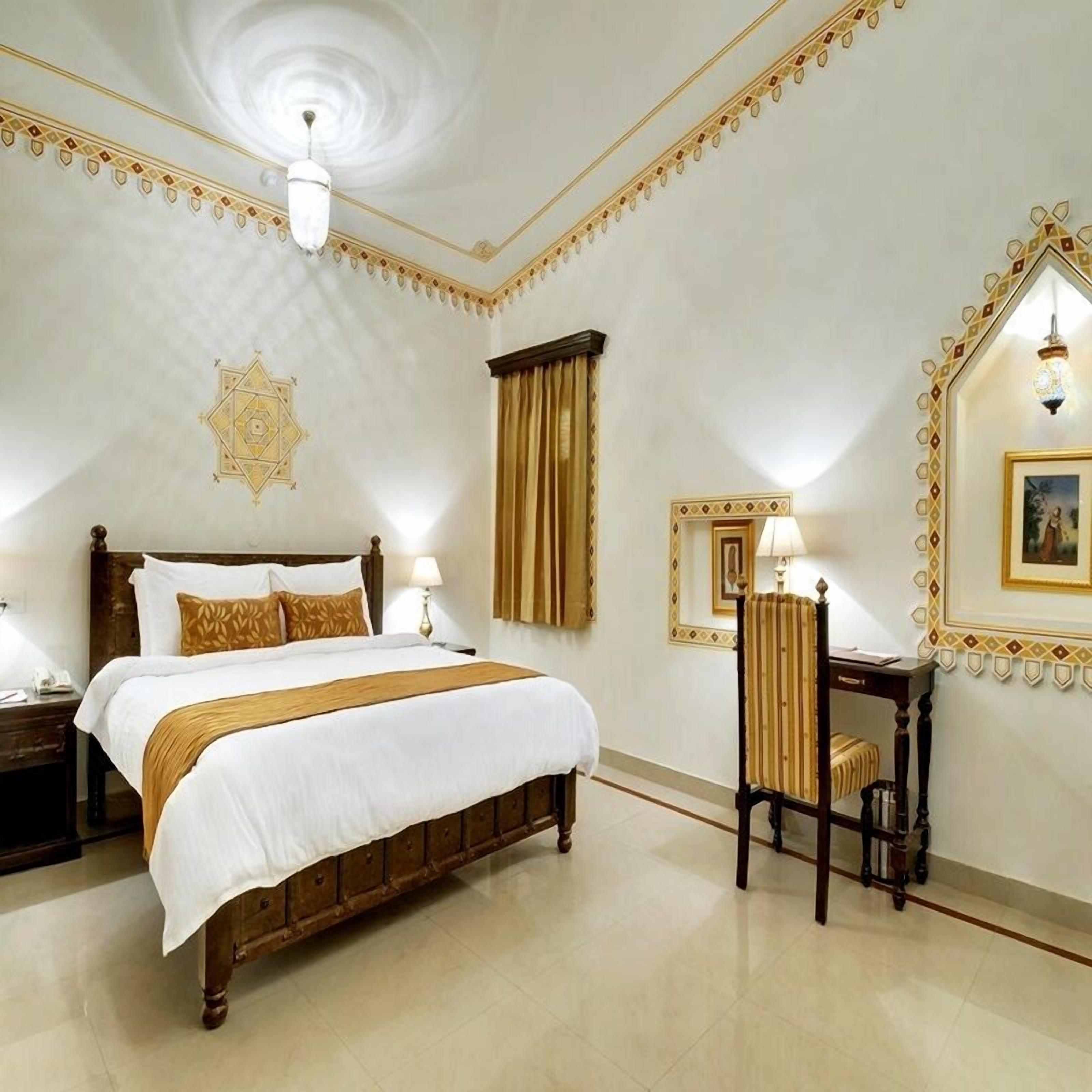 A hotel room with a large bed, a desk with a chair, and a decorative mirror.