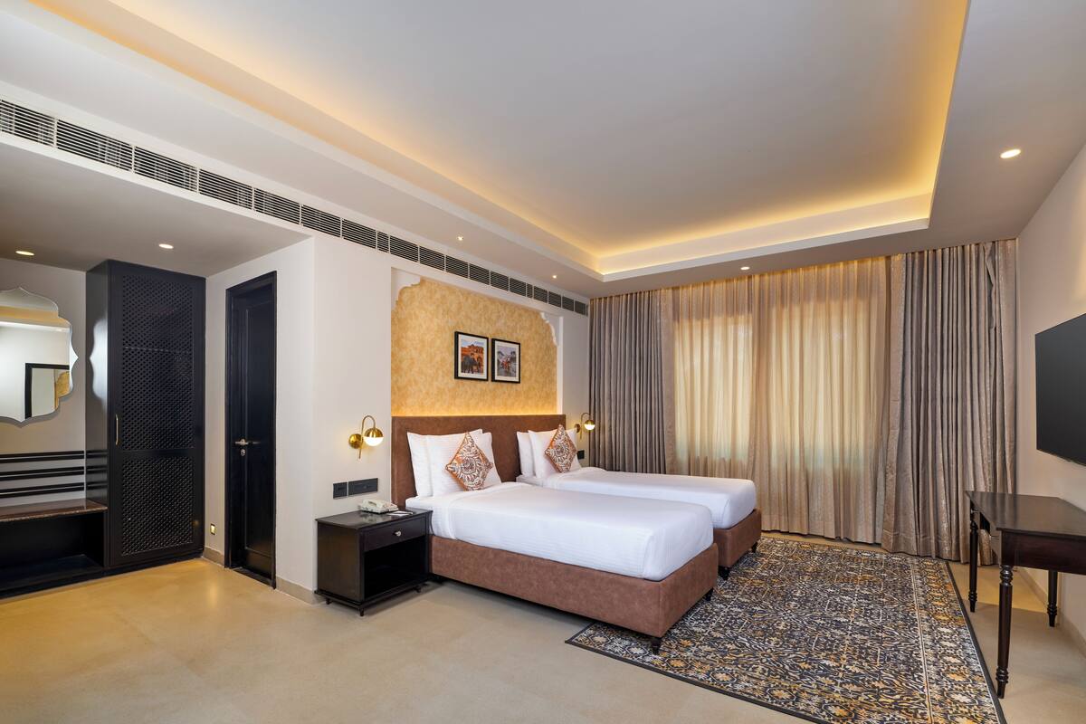 Quarto de hotel moderno com duas camas, um espelho grande, uma TV de tela plana e um tapete estampado.