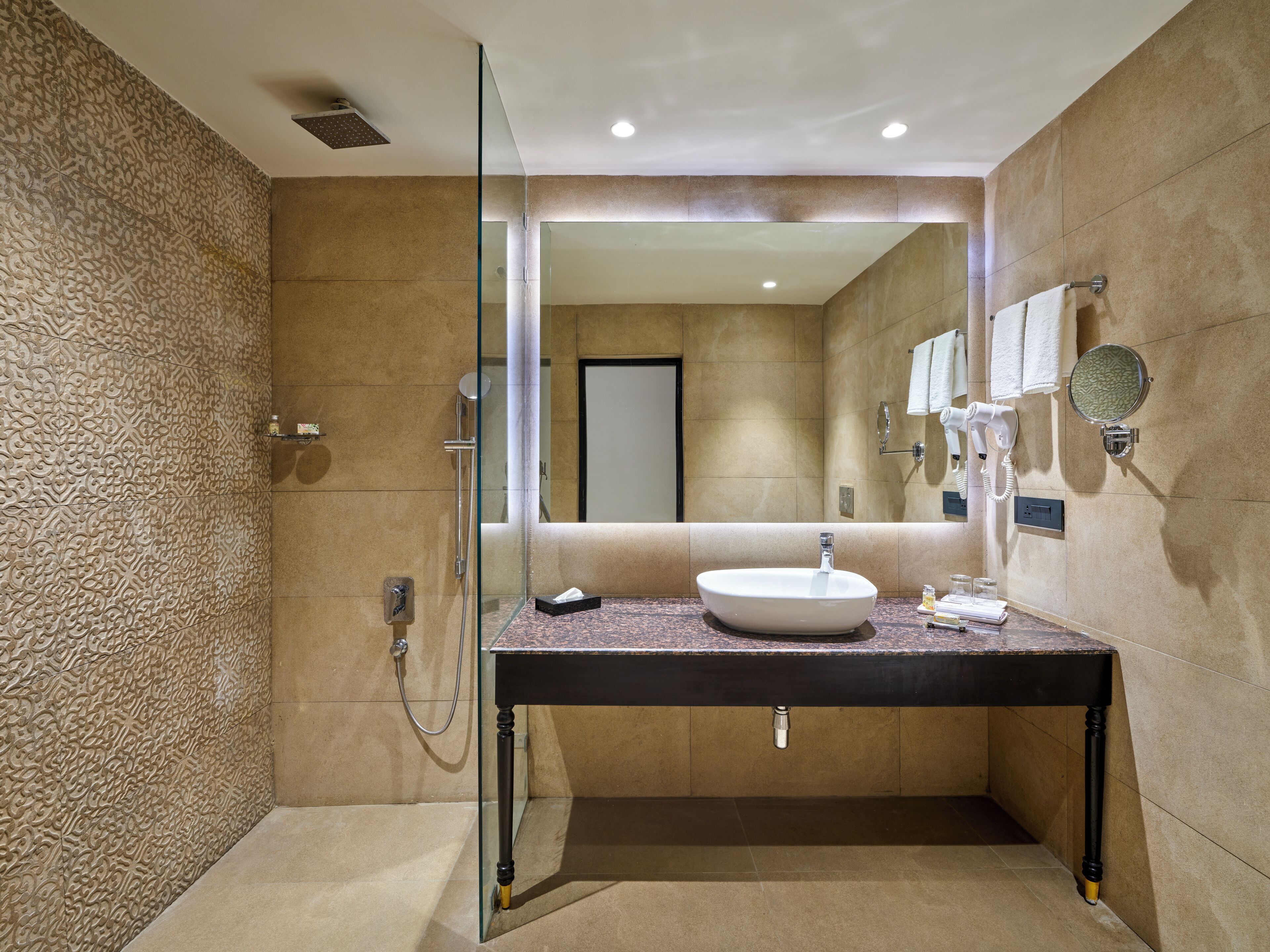 Un bagno moderno con doccia a vetro, lavabo rotondo e uno specchio grande.