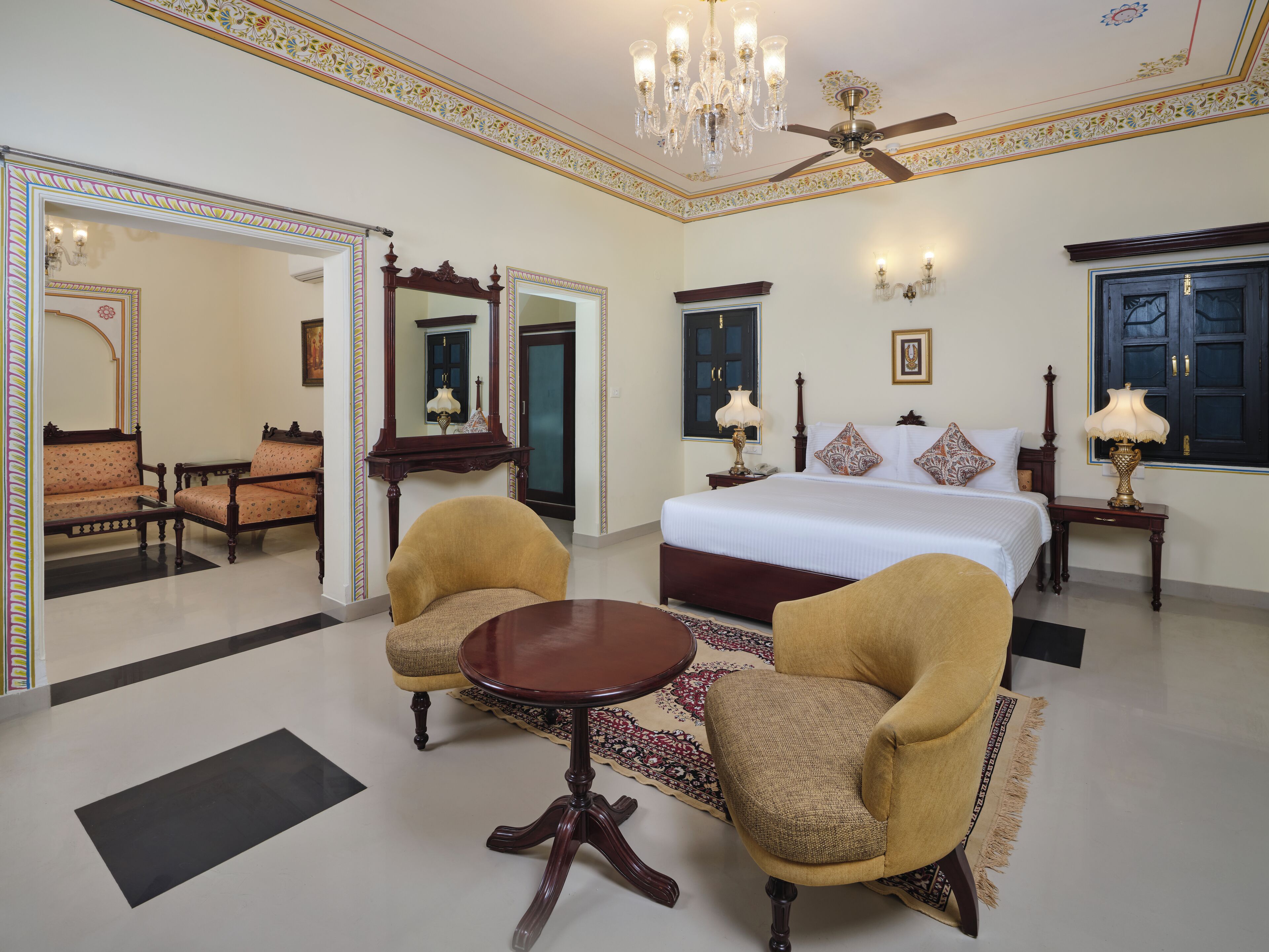 A spacious bedroom with a large bed, two armchairs, a round table, and a ceiling fan.