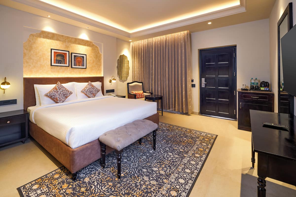 Quarto de hotel com uma cama grande, um banco, uma escrivaninha e um guarda-roupa.