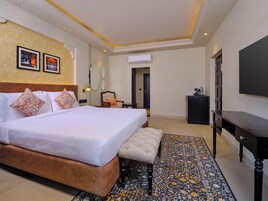 Una habitación de hotel con una cama grande, una banca, un televisor y un escritorio.