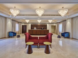 A spacious lobby with a reception desk, two blue armchairs, a red sofa, and three chandeliers.